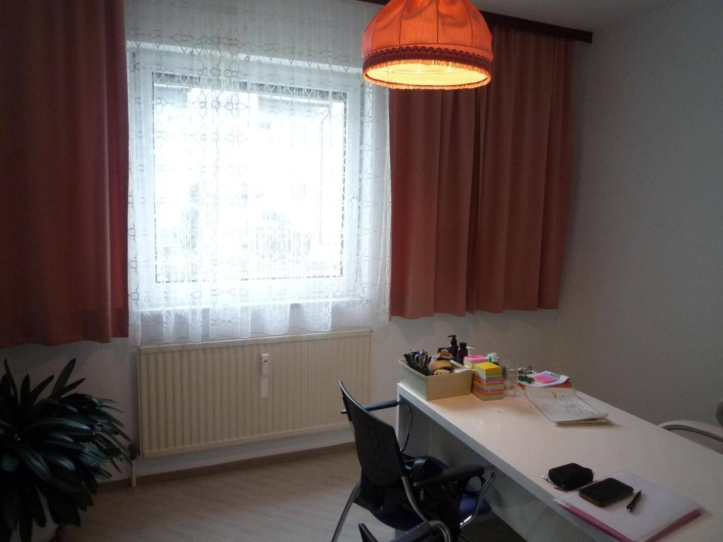 Arbeitszimmer mit Schreibtisch, Stuhl und einem Fenster mit Vorhängen und Heizkörper.