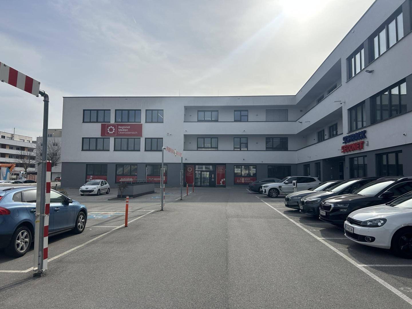 Ansicht eines modernen Geschäftsgebäudes mit vielen Fenstern und einem geräumigen Parkplatzbereich.