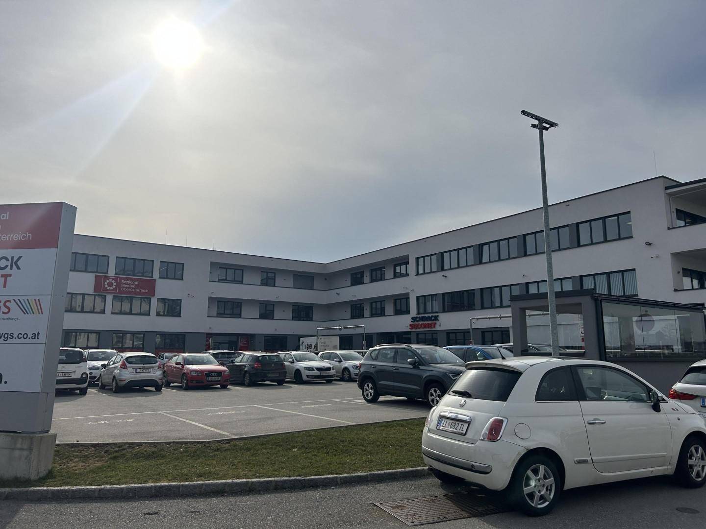 Weitläufiger Blick auf das moderne Bürogebäude und den Parkplatz, beleuchtet von der Sonne.