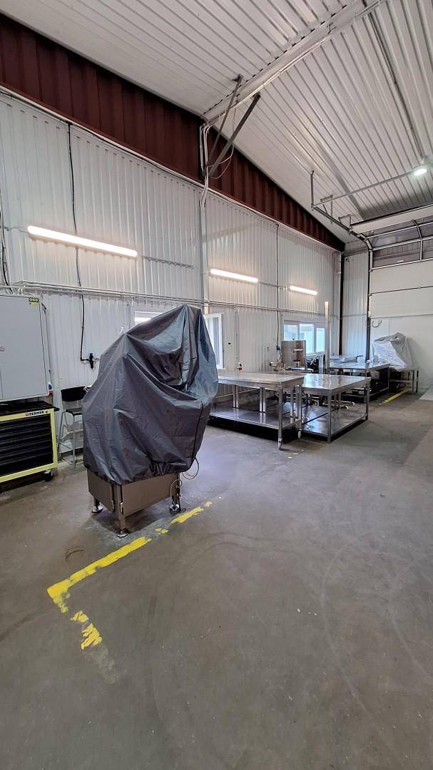 Industrielle Lagerhalle mit hohen Decken, Metalltischen und einer abgedeckten Maschine.