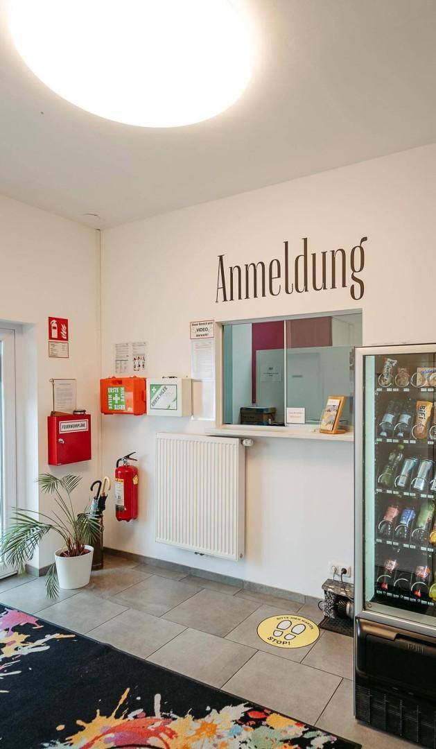 Empfangsbereich mit Anmeldeschalter, Verkaufsautomat und Sicherheitsausrüstung an der Wand.