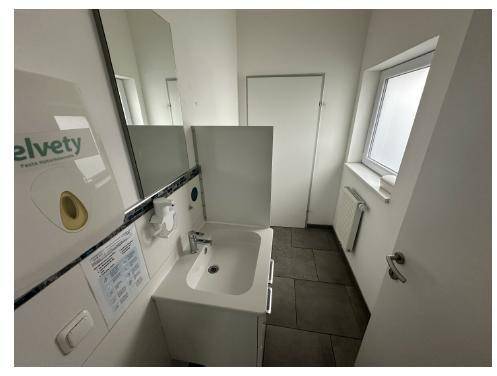 Helles Badezimmer mit Waschbecken, Spiegel und Fenster, ausgestattet mit Fliesenboden.