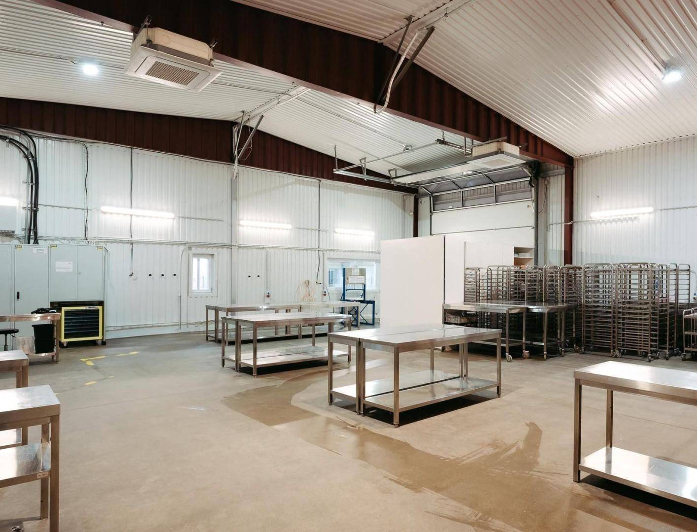 Große Lagerhalle mit hohen Decken, Metalltischen und einem Rolltor im Hintergrund.