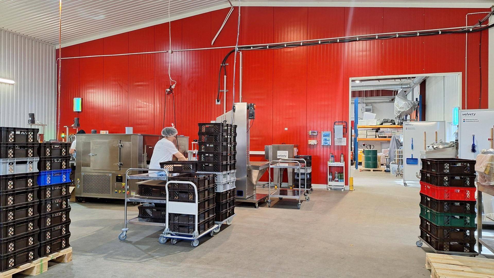 Produktionsbereich mit roten Wänden, Maschinen und gestapelten Kisten, bereit für die Verarbeitung.