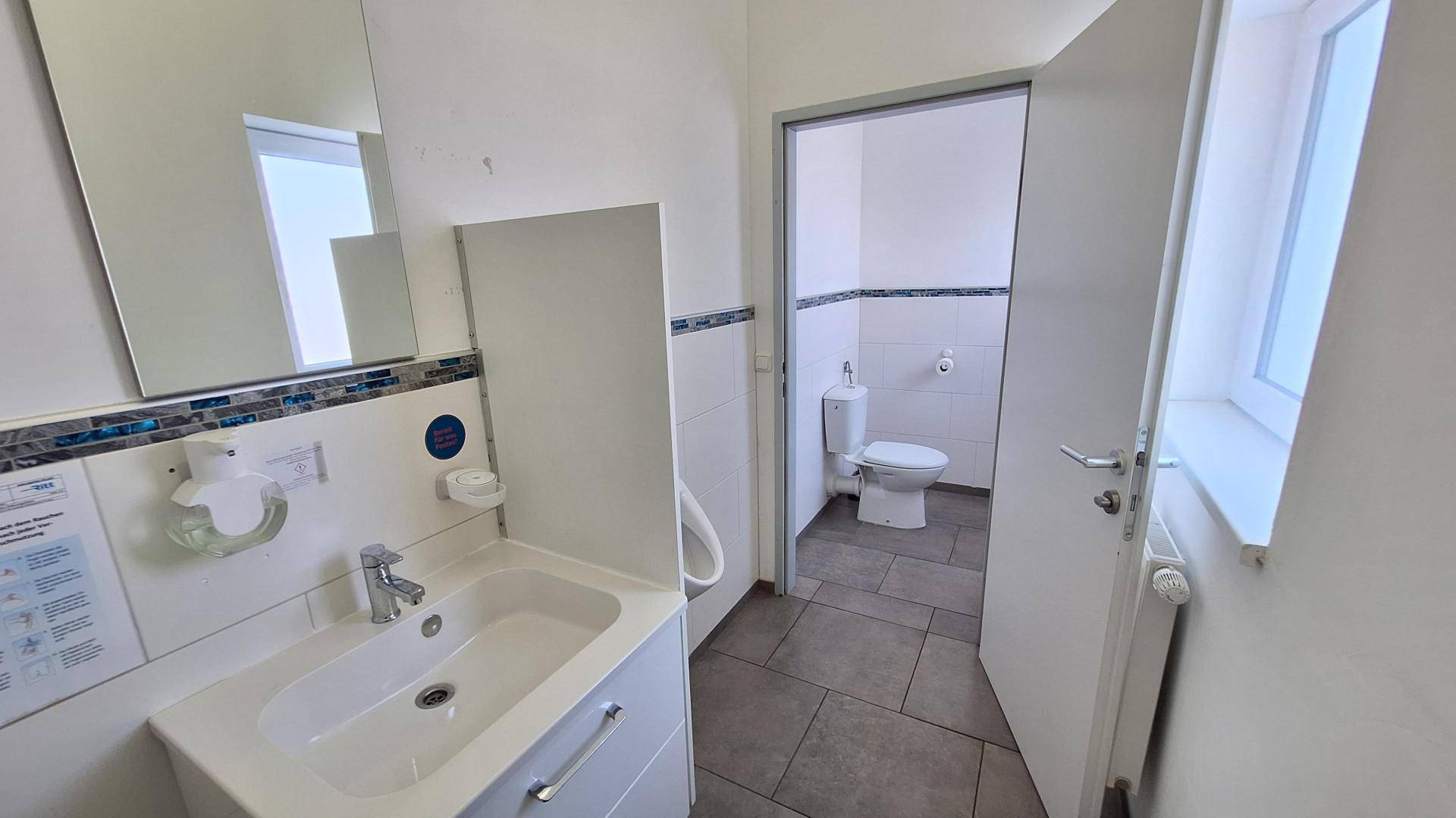 Helles Badezimmer mit Waschbecken, Spiegel und Fenster, mit Blick auf eine separate Toilette.