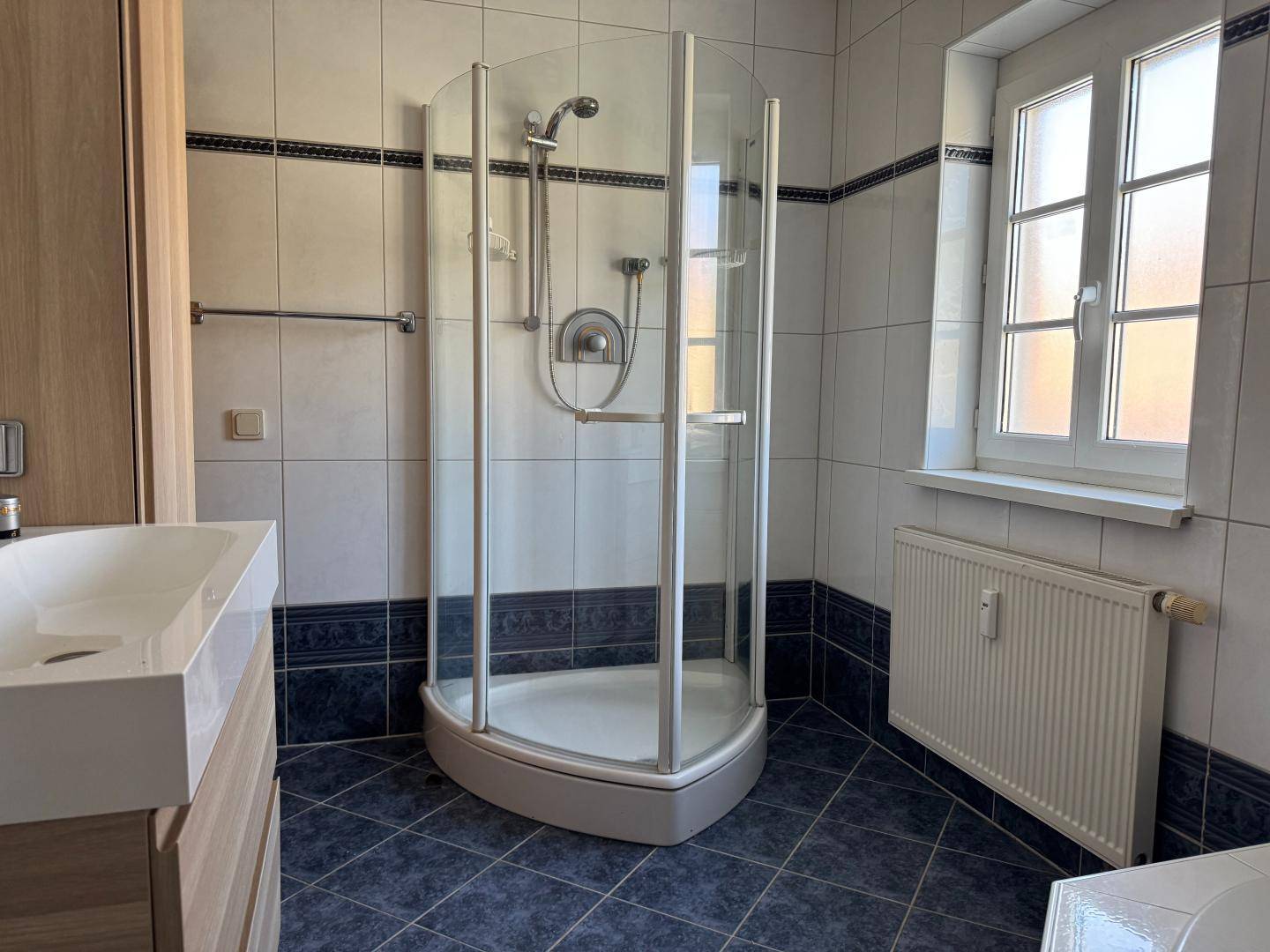 Badezimmer mit Duschkabine, modernem Waschbecken und Fenster, das für gute Belüftung sorgt.