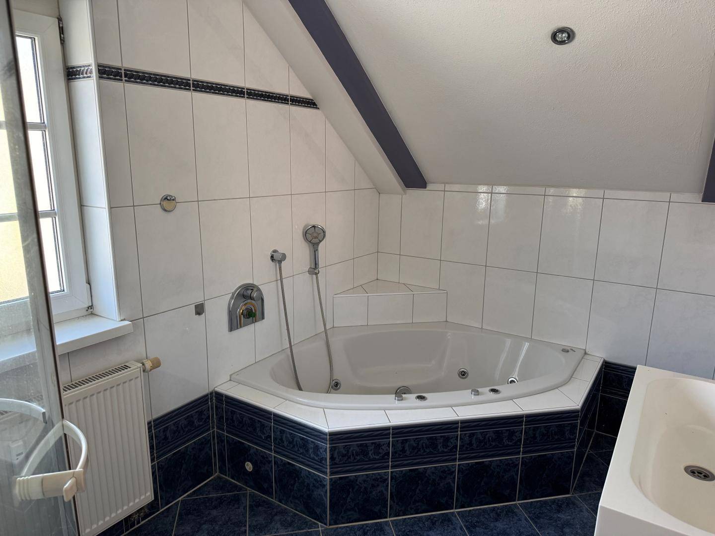 Badezimmer im Dachgeschoss mit Eckbadewanne und blauen Fliesen, bietet Entspannung nach einem langen Tag.