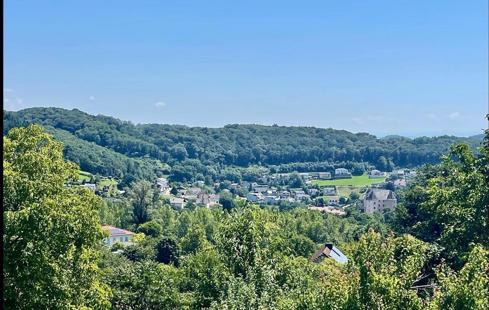 Idyllischer Blick auf die bewaldeten Hügel und ein kleines Dorf in der Ferne.