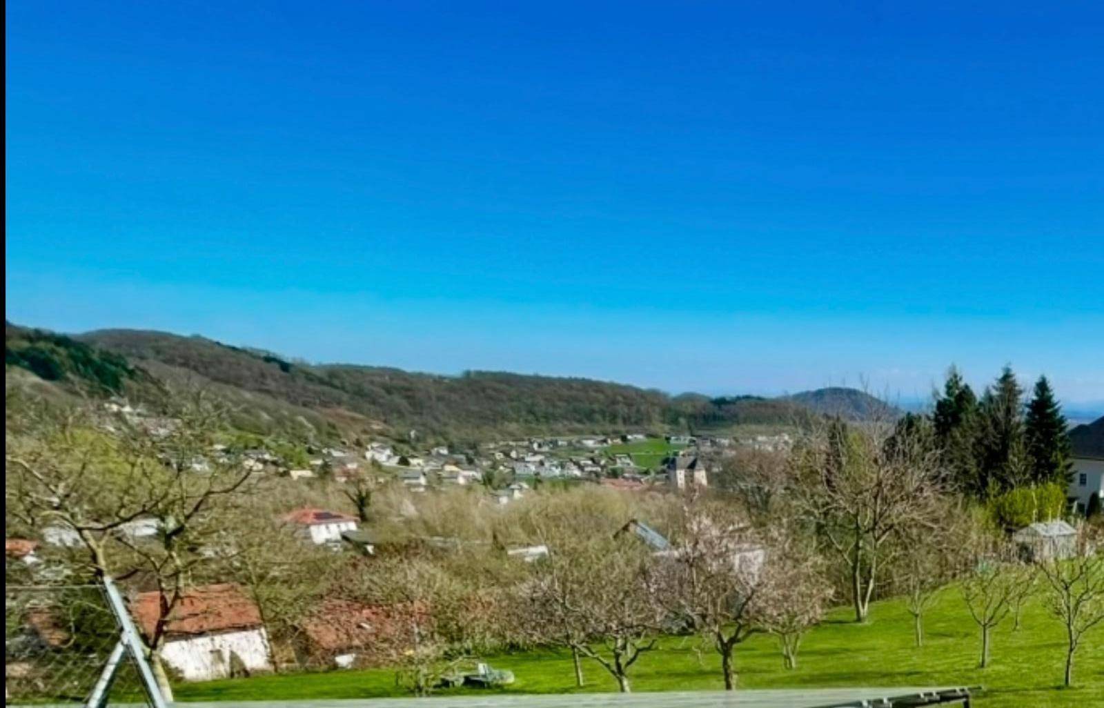 Sonniger Ausblick über die sanften Hügel und ein charmantes Dorf im Tal.