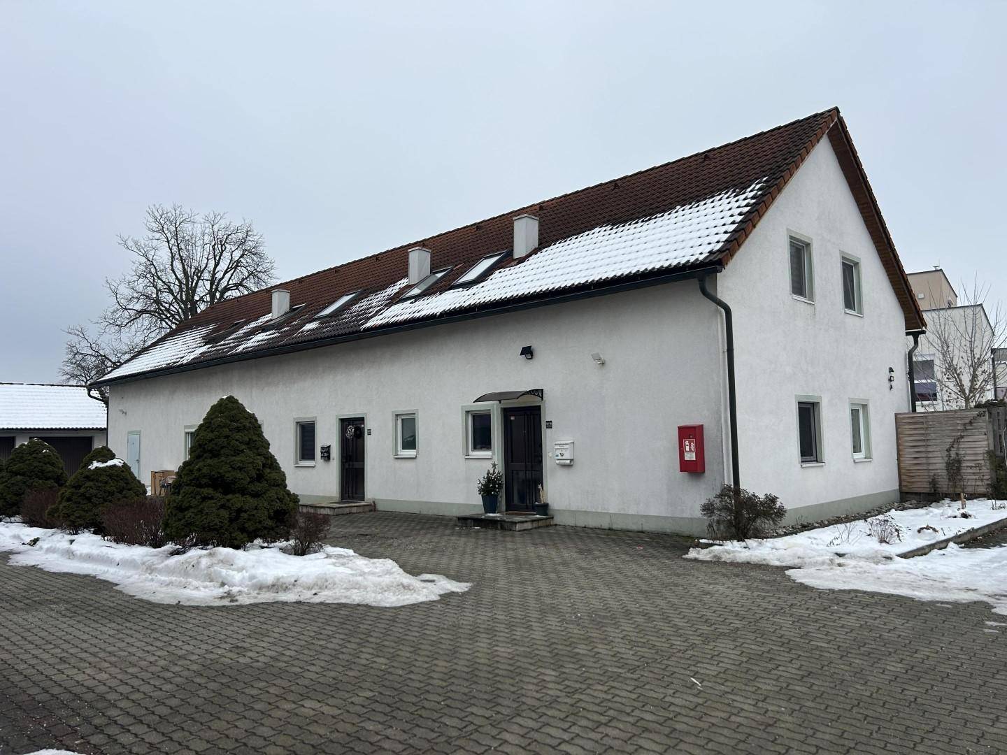 Vorderansicht eines weißen Gebäudes mit mehreren Eingängen und verschneitem Dach im Winter.