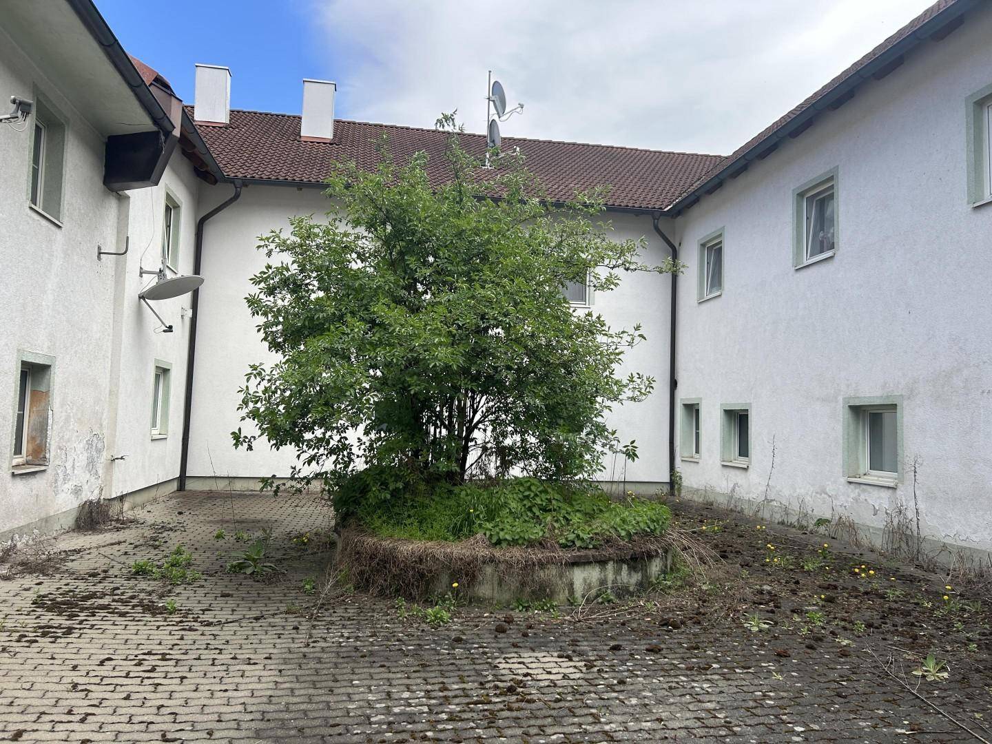 Innenhof mit einem Baum in der Mitte, umgeben von Gebäuden mit weißen Fassaden.