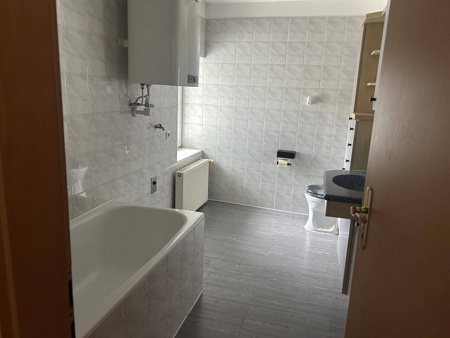 Gefliestes Badezimmer mit Badewanne, Toilette und Fenster für natürliche Belüftung.