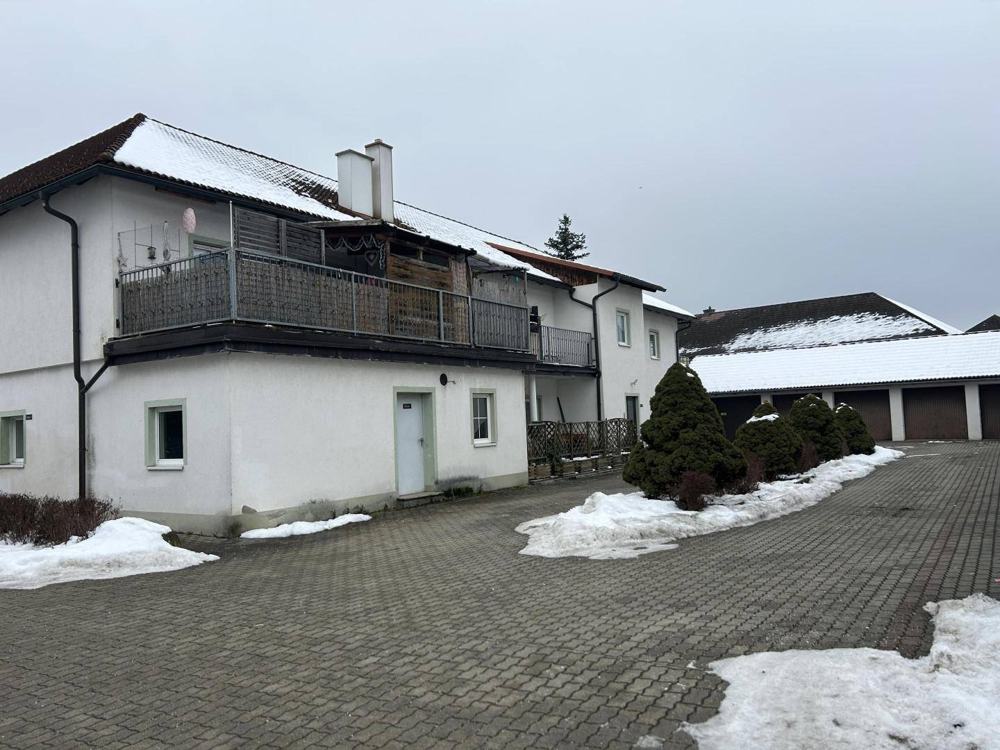 Großer Balkon an der Rückseite eines weißen Gebäudes mit Blick auf Garagen und verschneite Flächen.