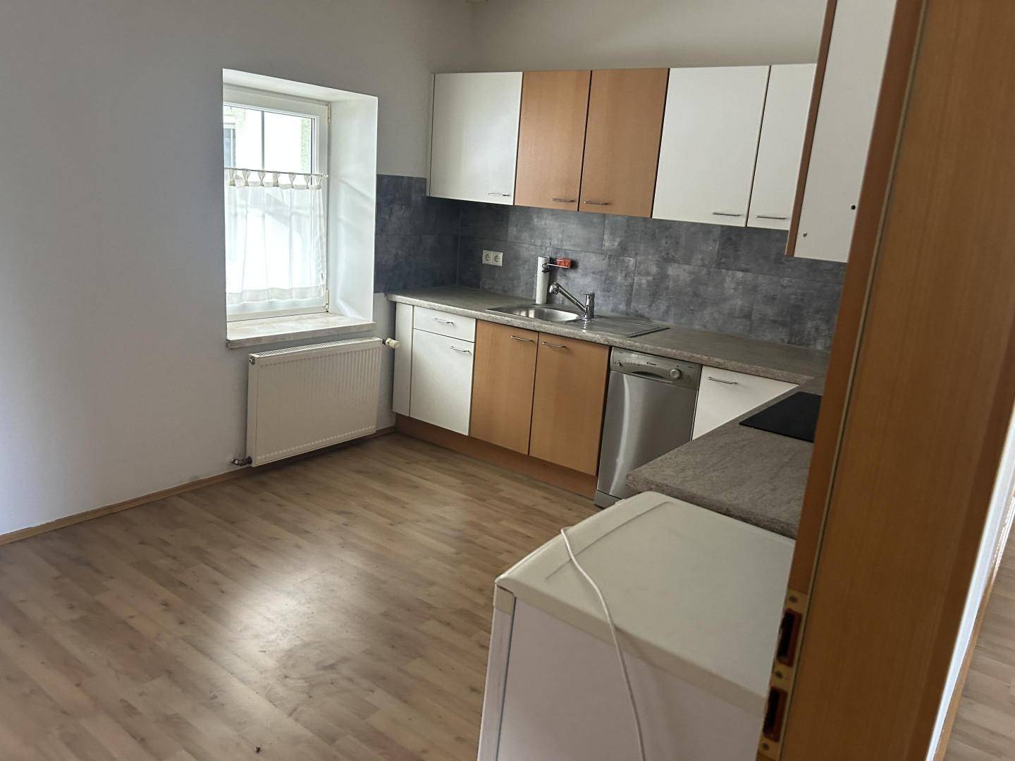 Funktionale Küche mit zweifarbigen Schränken, Spüle und Fenster mit Blick nach draußen.