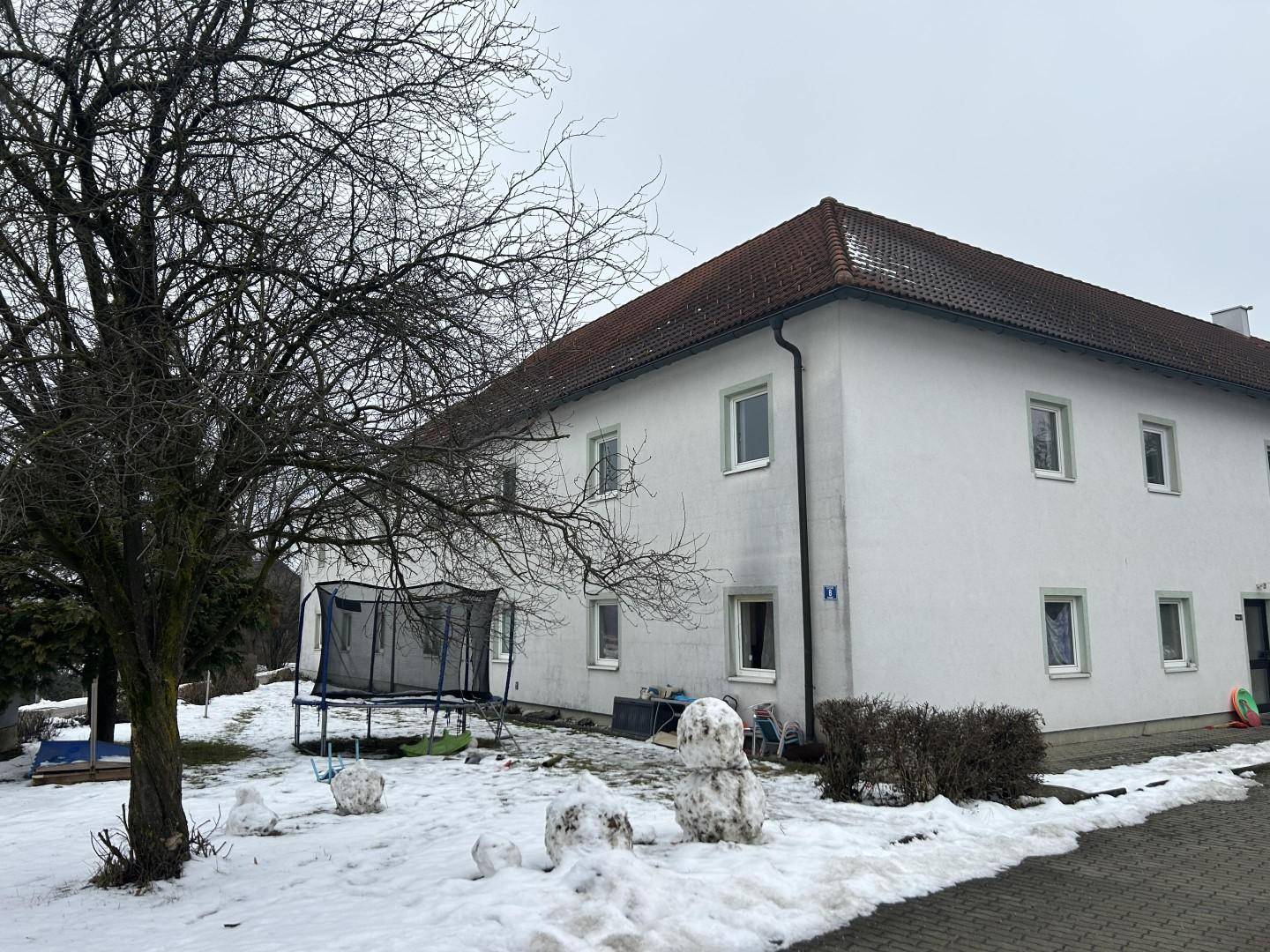 Seitenansicht eines weißen Gebäudes mit einem Trampolin im verschneiten Gartenbereich.