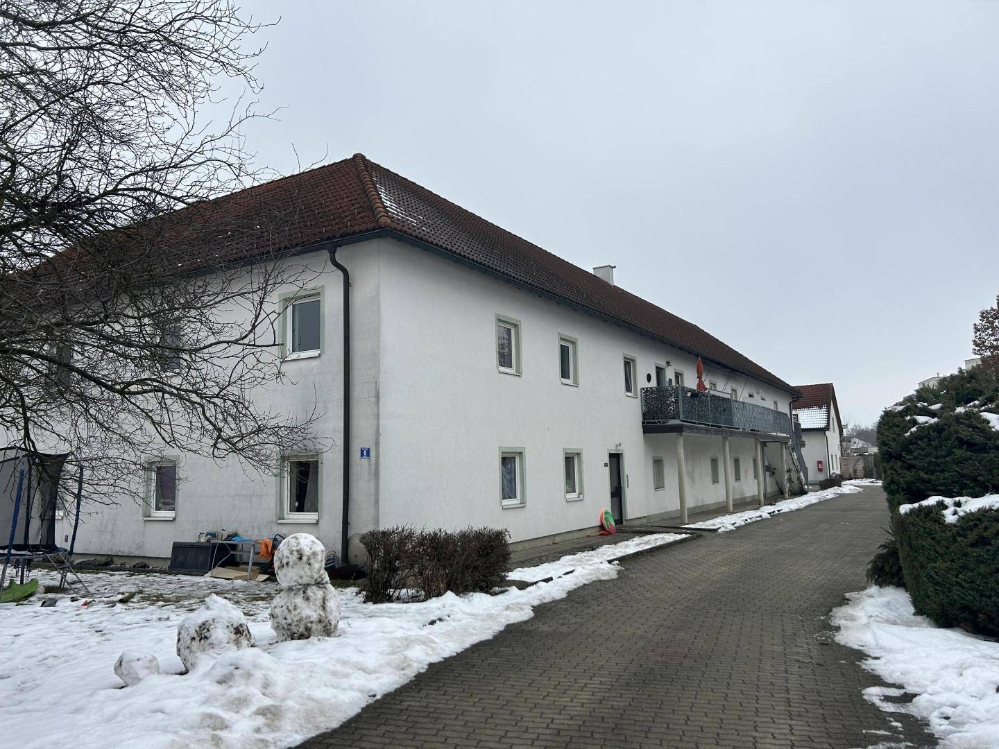 Seitenansicht eines weißen Gebäudes mit Balkonen und verschneiter Umgebung im Winter.