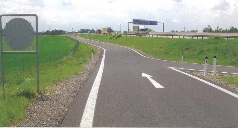 Asphaltierte Zufahrtsstraße mit weißen Markierungen, die zu einer Autobahn im Hintergrund führt.