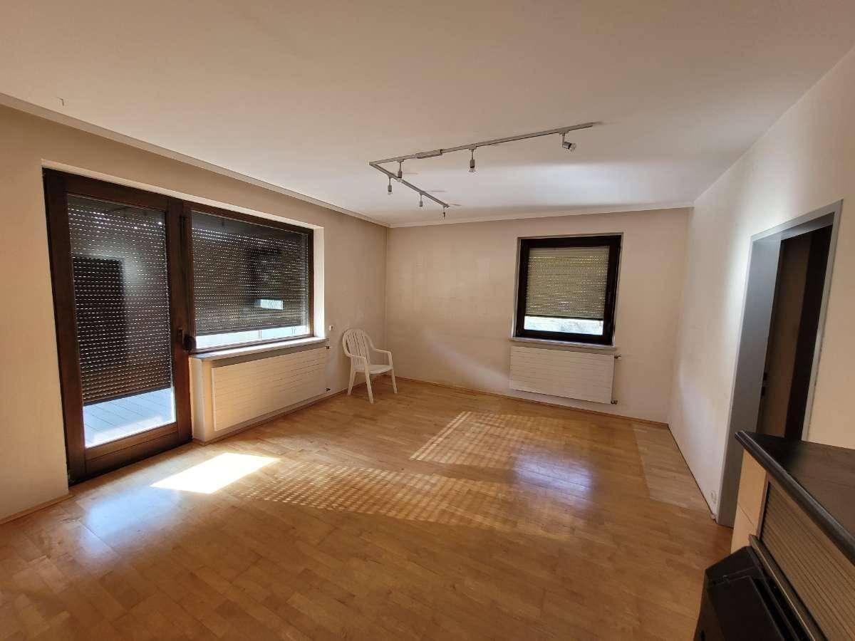 Geräumiges Wohnzimmer mit Parkettboden, viel Tageslicht und Zugang zum Balkon.