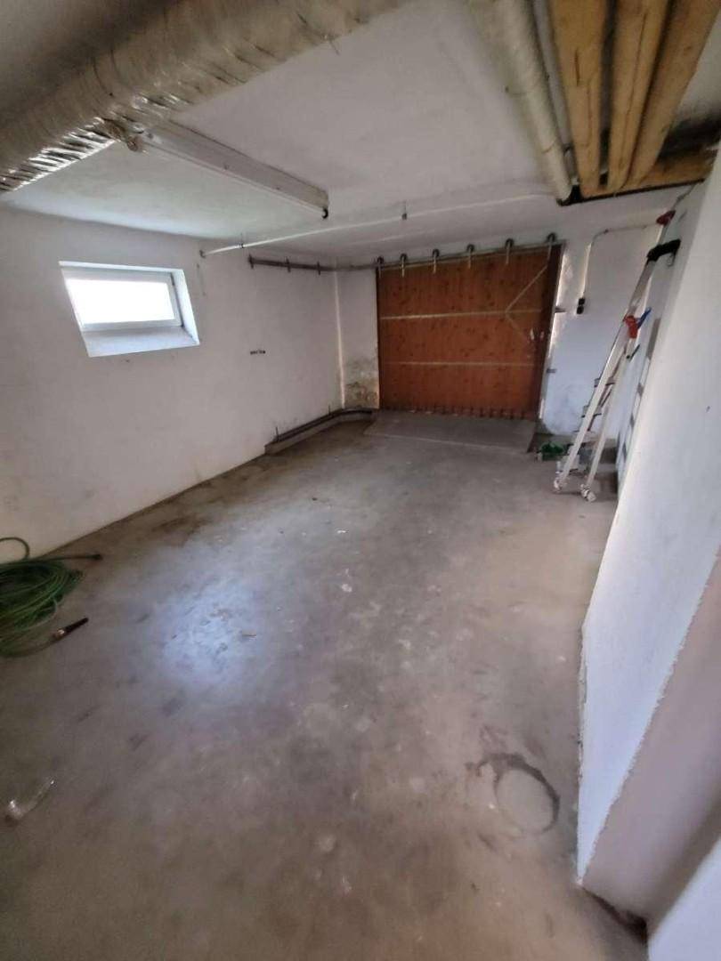 Geräumige Garage mit Betonboden, Fenster und großem Holztor.