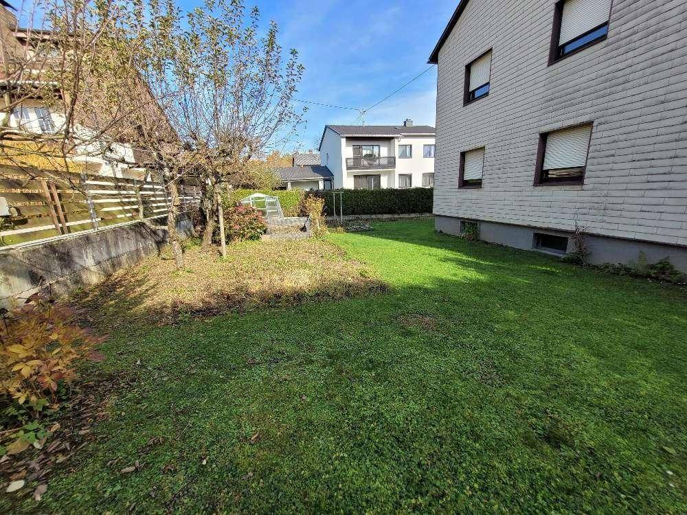 Gepflegter Gartenbereich mit Rasenfläche und Blick auf die Hausfassade unter blauem Himmel.