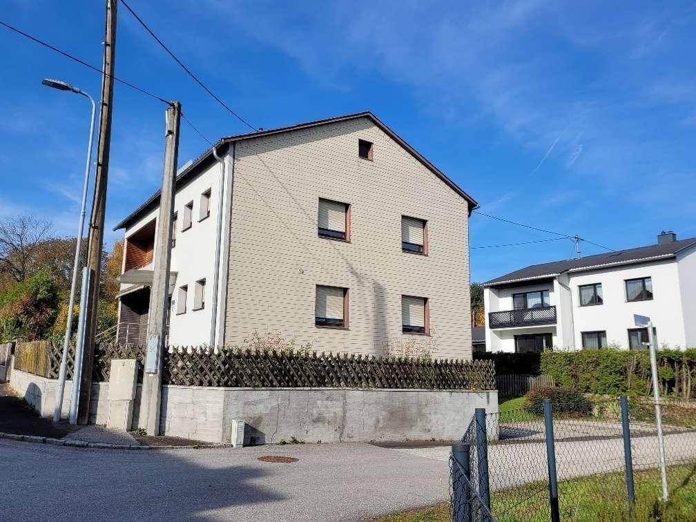 Ansicht des Hauses von der Straße mit heller Fassade und Fenstern mit Rollläden.