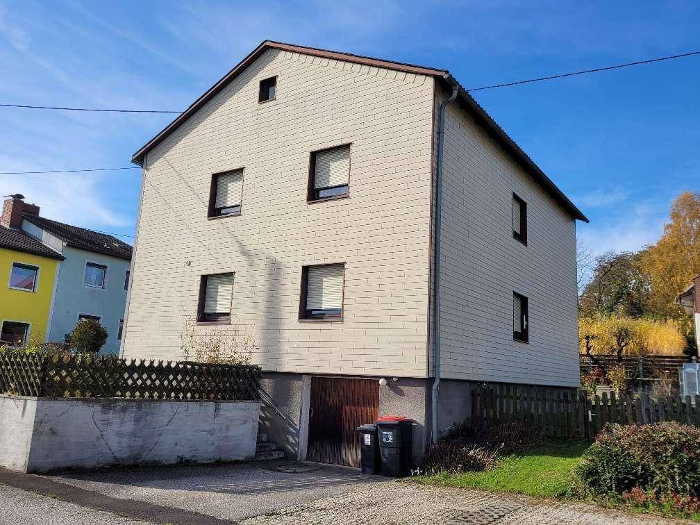 Seitenansicht des Hauses mit Garagentor, heller Fassade und Satteldach.