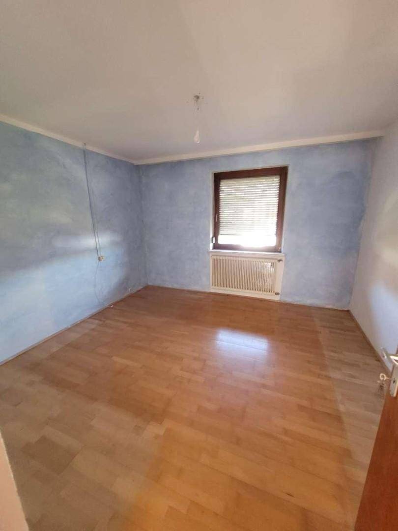 Schlafzimmer mit blauer Akzentwand, Parkettboden und Fenster mit Rollladen.