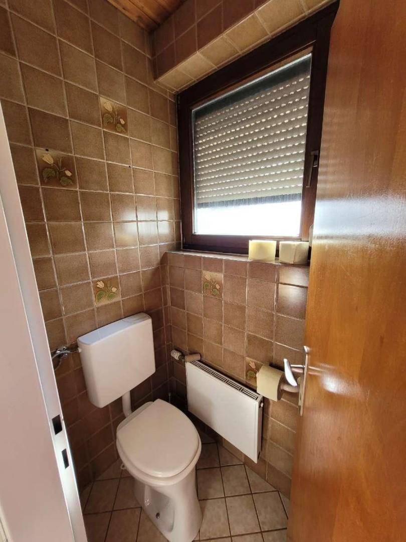 Gäste-WC mit braunen Fliesen, Fenster und Holzdecke.