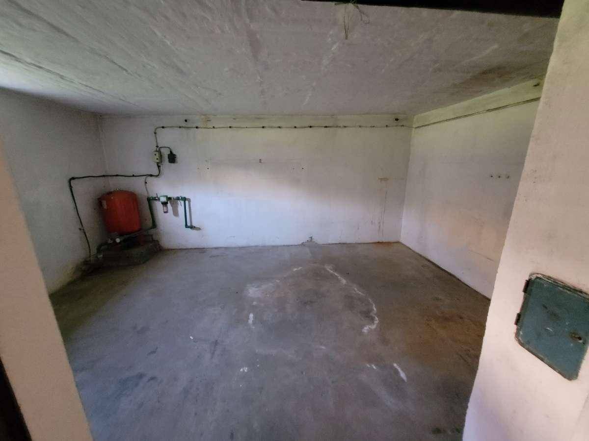 Kellerraum mit Betonboden, weiß gestrichenen Wänden und Wasserinstallationen.