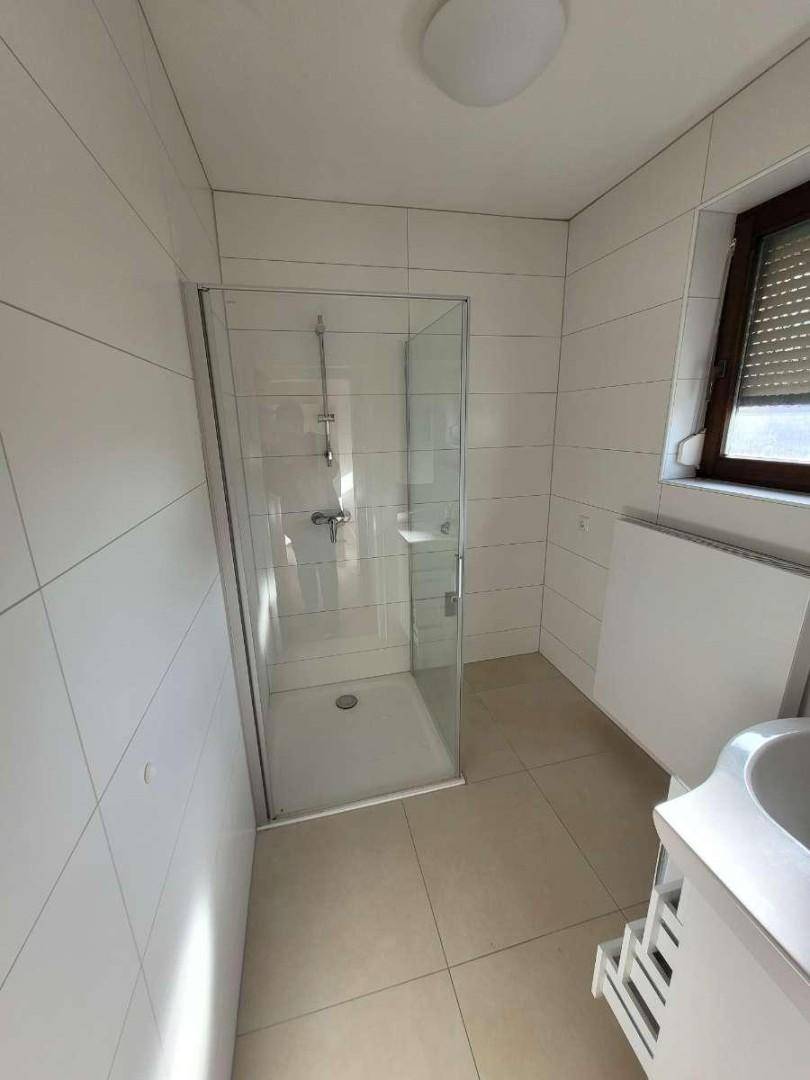Modernes Badezimmer mit weiß gefliesten Wänden, Duschkabine und Fenster.