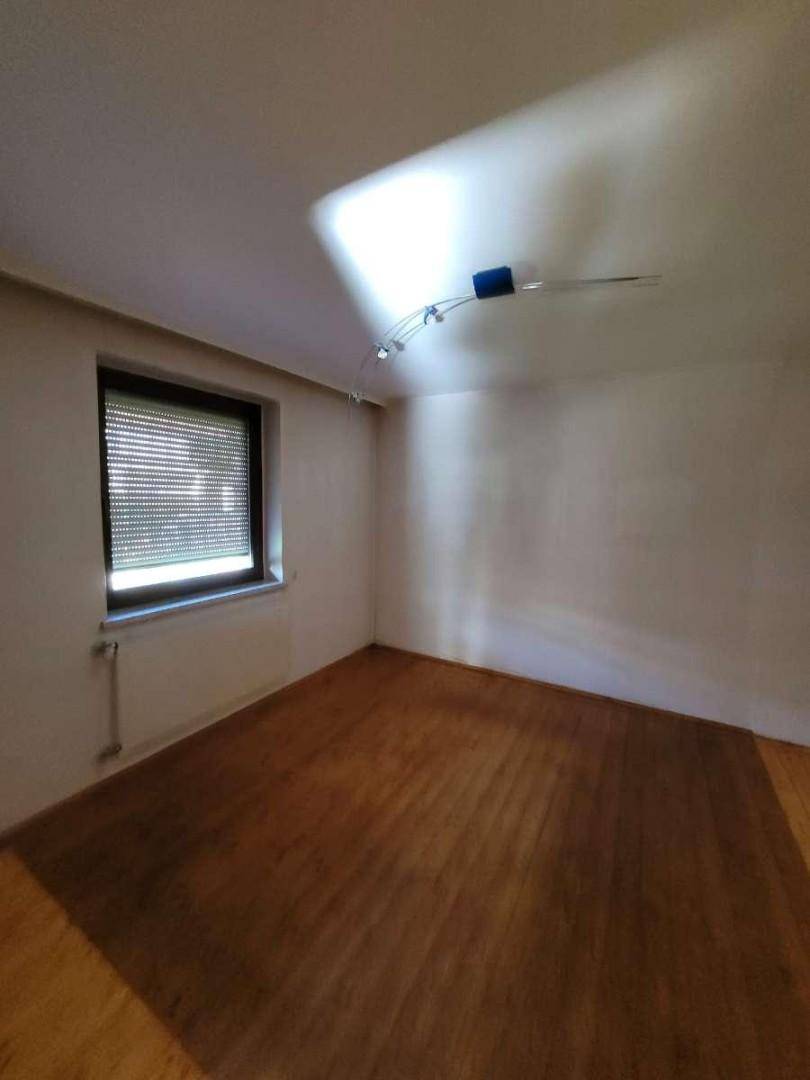 Helles Zimmer mit Parkettboden, weißen Wänden und Fenster mit Rollladen.