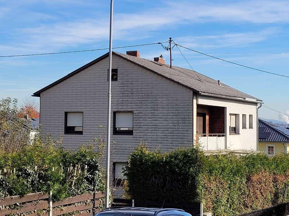 Seitenansicht des Hauses mit Balkon, Satteldach und umgebender Vegetation.