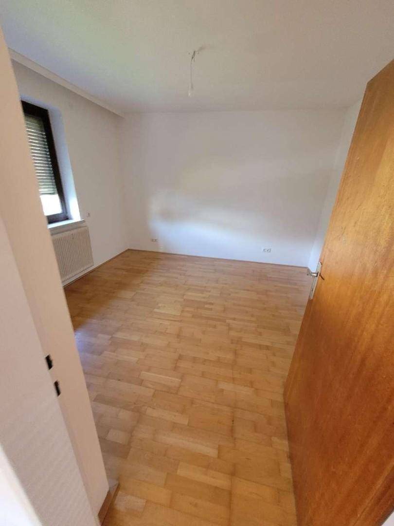 Helles Schlafzimmer mit Parkettboden, weißen Wänden und Fenster mit Rollladen.