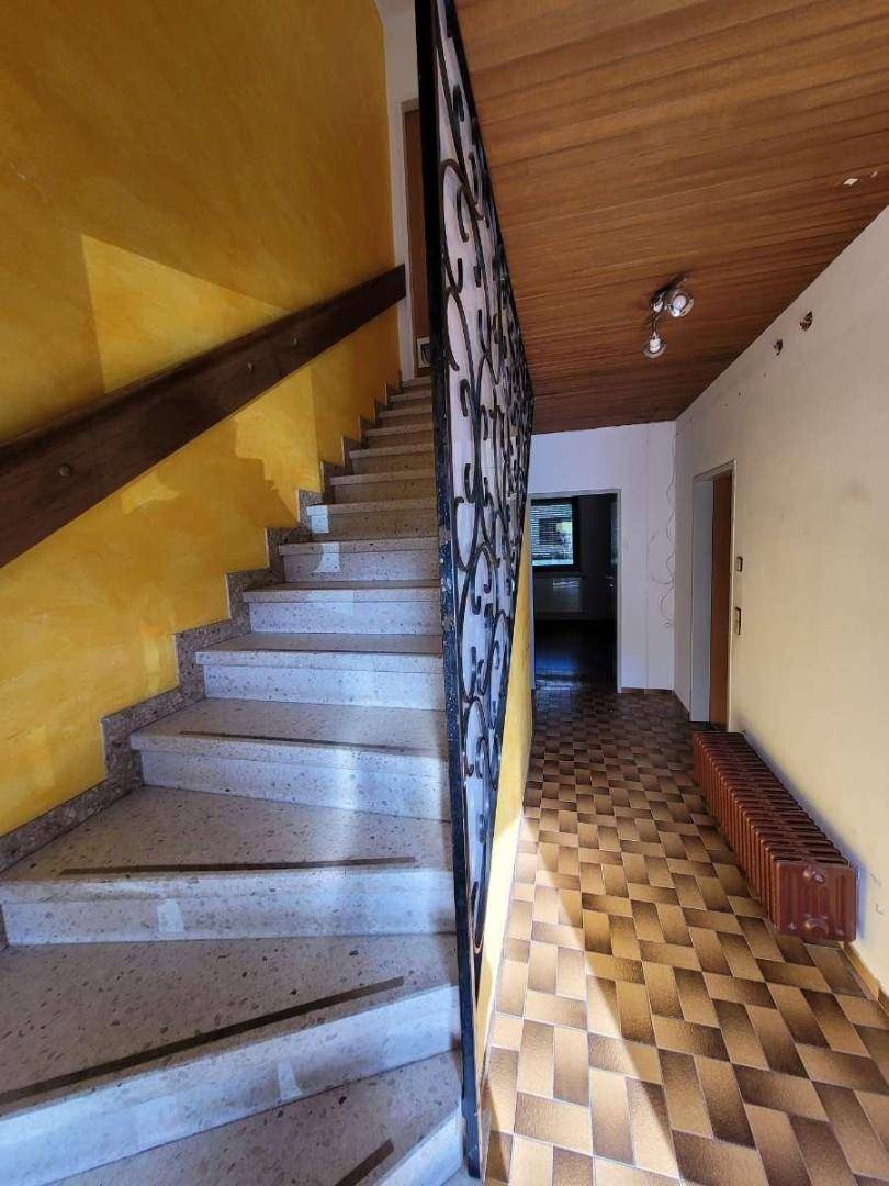 Flur mit Steintreppe, schmiedeeisernem Geländer und Holzdecke.