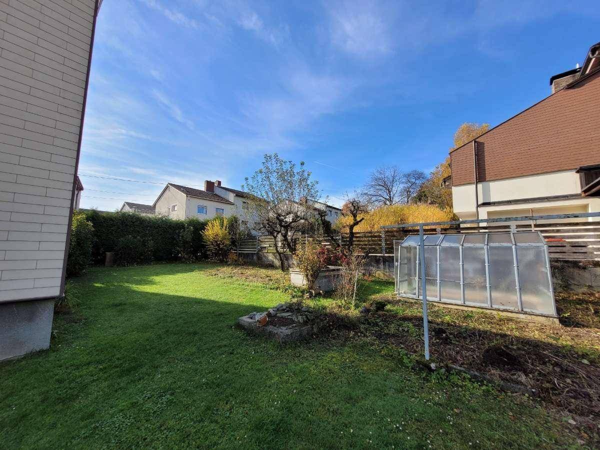 Großer Gartenbereich mit Rasenfläche, Bäumen und einem kleinen Gewächshaus.