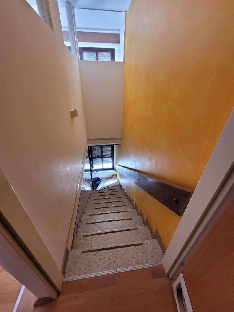Treppenhaus mit Steinstufen, gelben Wänden und Holzgeländer.