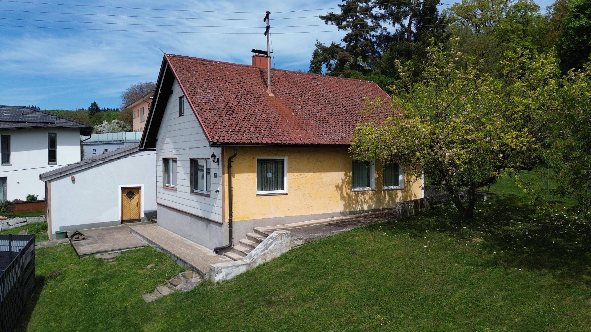 Ansicht des Einfamilienhauses mit gelber Fassade, rotem Ziegeldach und grünem Vorgarten.