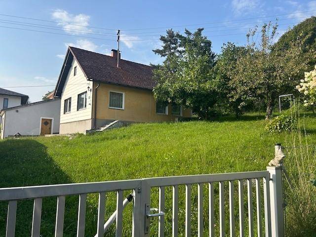 Blick auf das Einfamilienhaus mit großem Gartenbereich, gesehen durch ein weißes Gartentor.