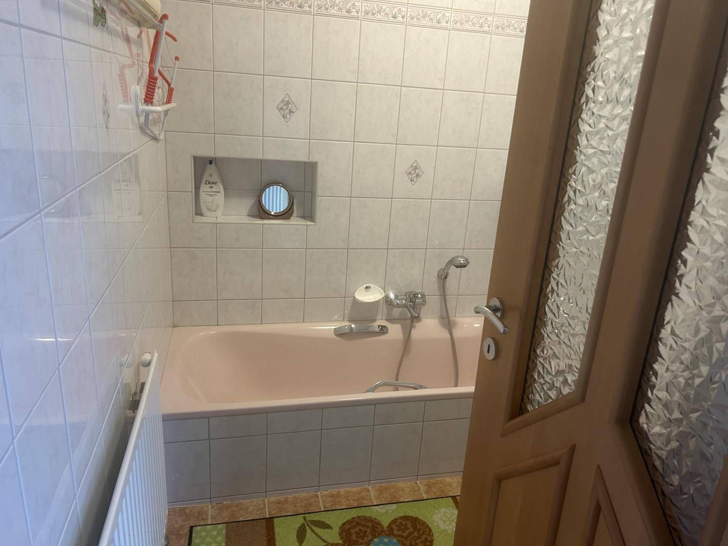Badezimmer mit rosa Badewanne, weißen Fliesen und integrierter Nische für Ablagen.