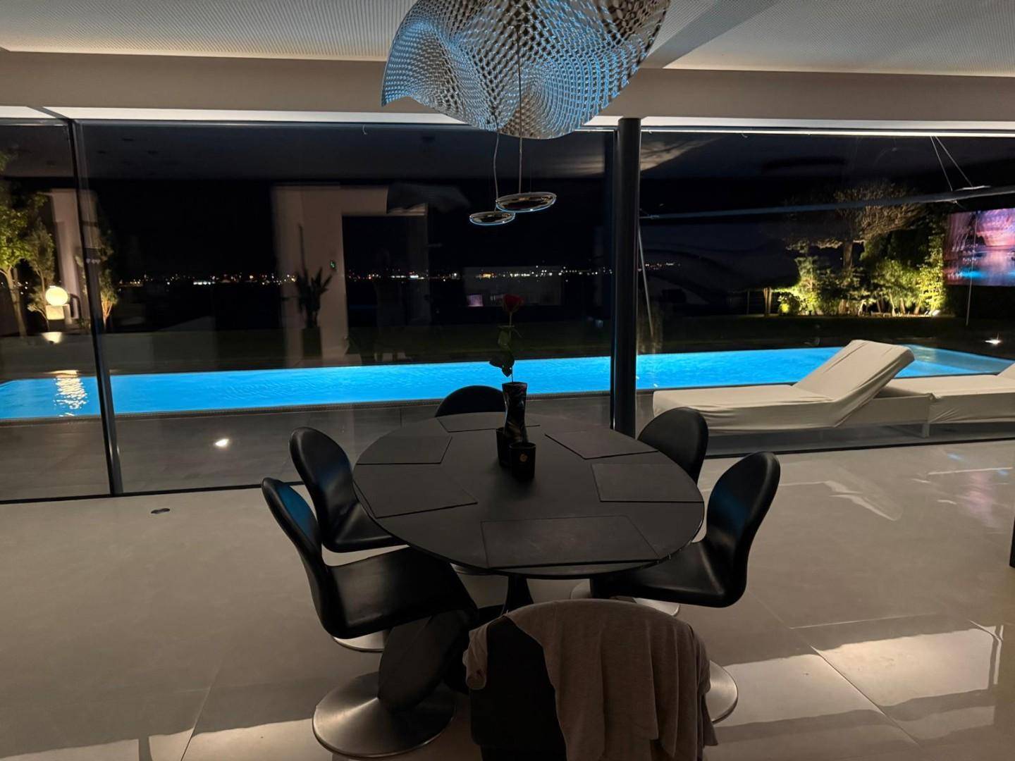 Moderner Essbereich mit Blick auf den beleuchteten Pool und die nächtliche Landschaft.
