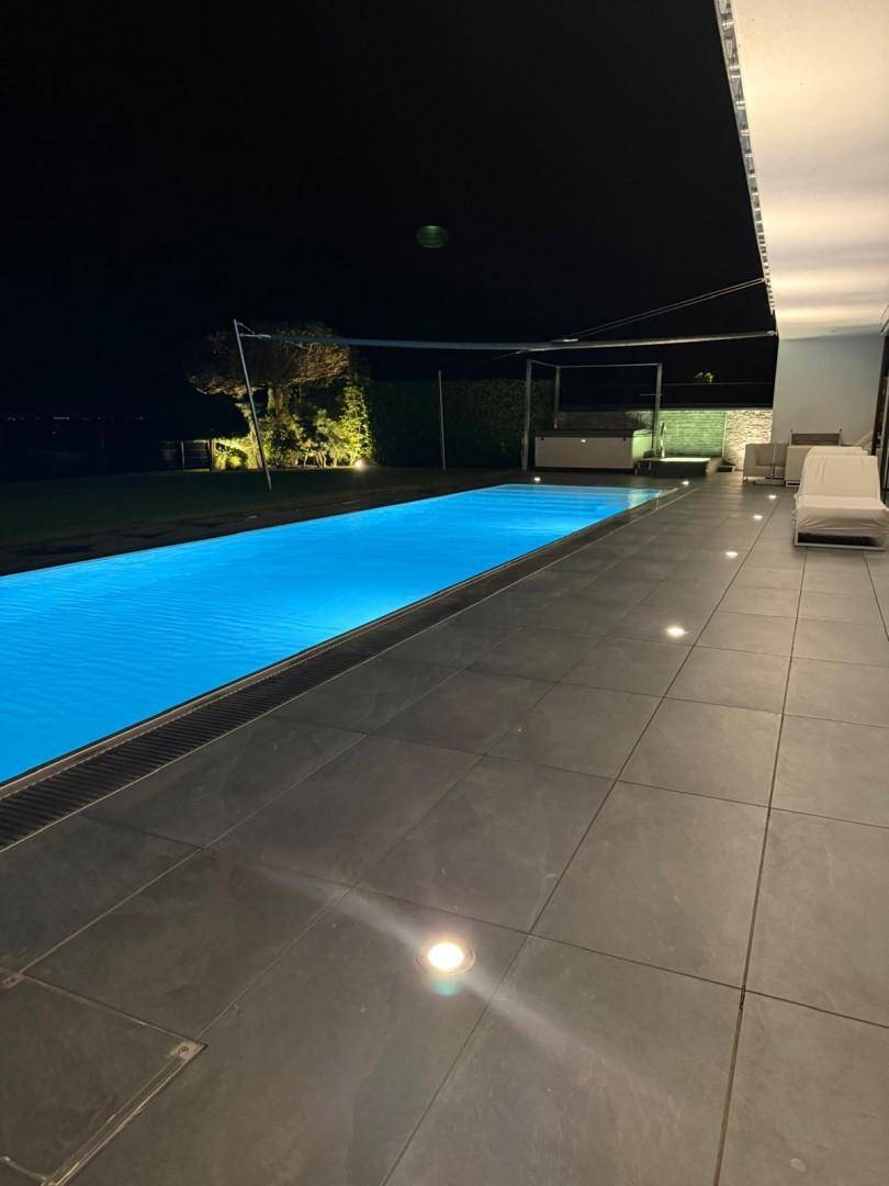 Großzügige geflieste Terrasse mit einem langen, beleuchteten Swimmingpool bei Nacht.