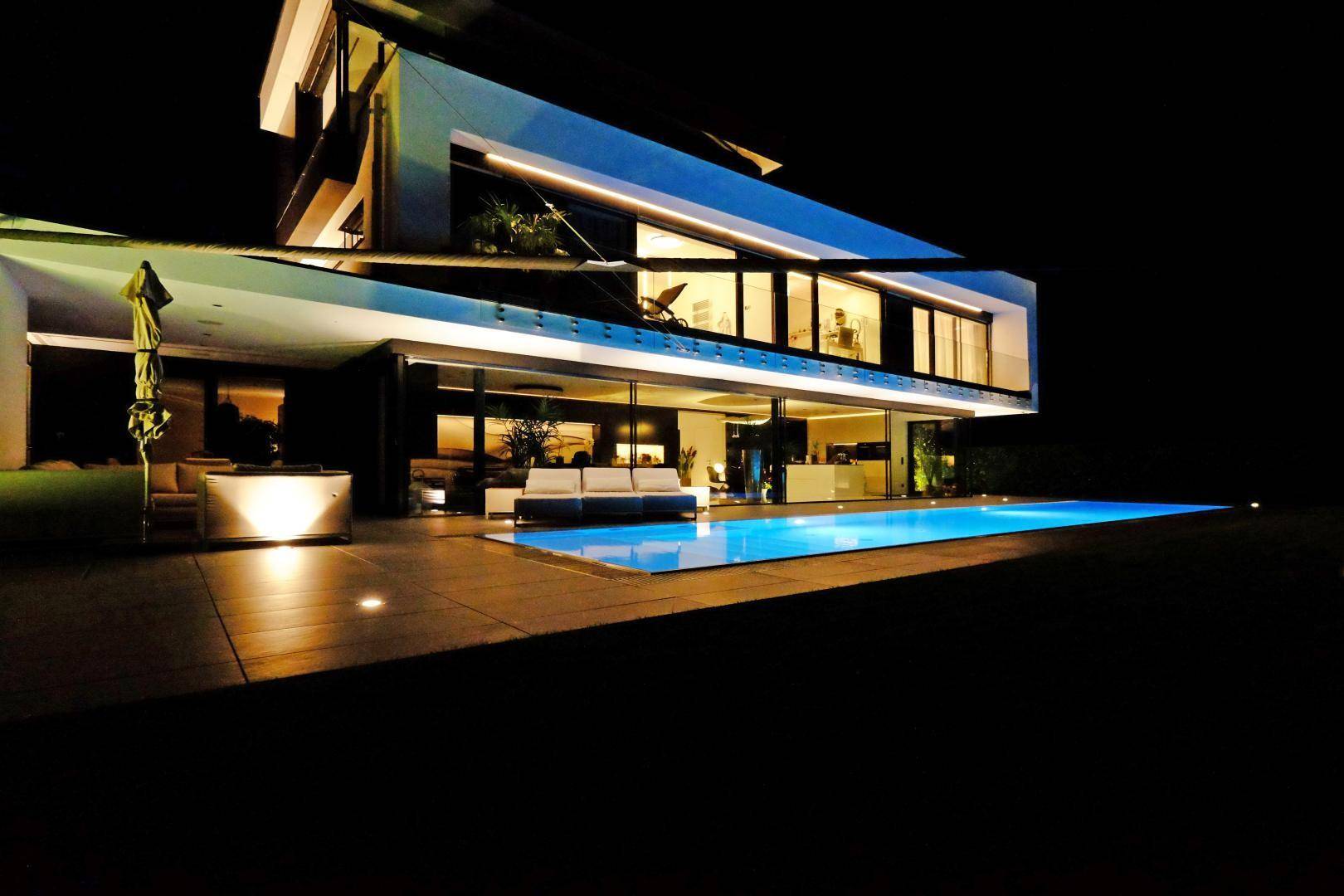 Luxuriöse Terrasse mit beleuchtetem Pool und stilvollen Outdoor-Möbeln bei Nacht.