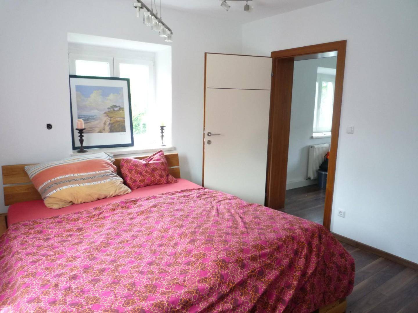 Gemütliches Schlafzimmer mit Holzbett, dunklem Laminatboden und einem Fenster.