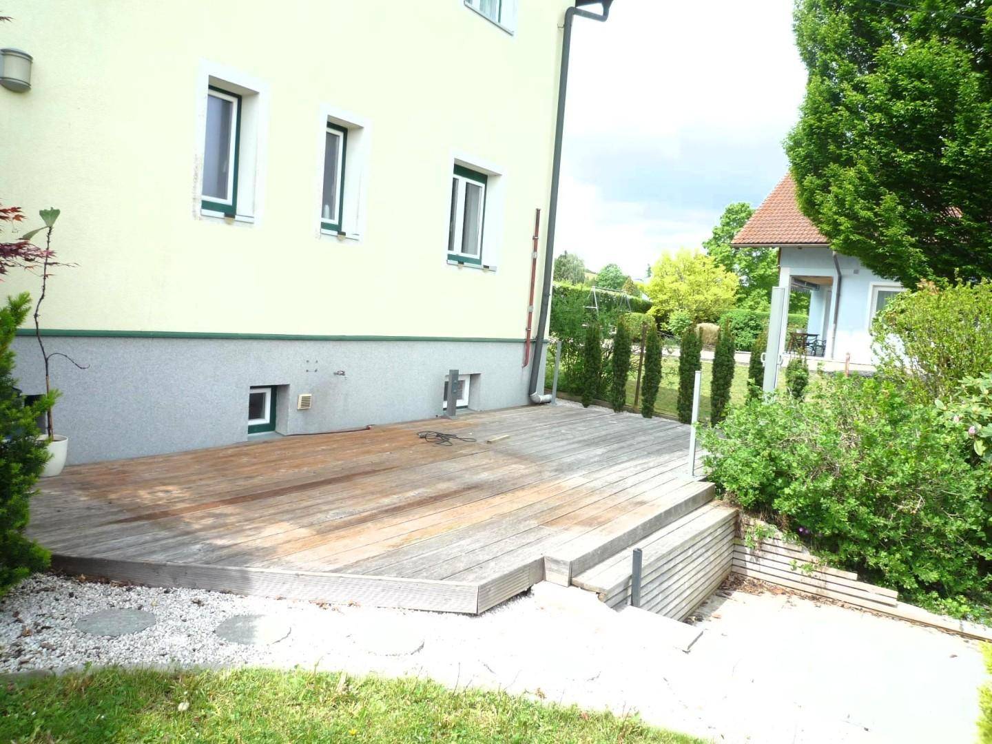 Große Holzterrasse am Haus mit Stufen, die in den grünen Garten führen.