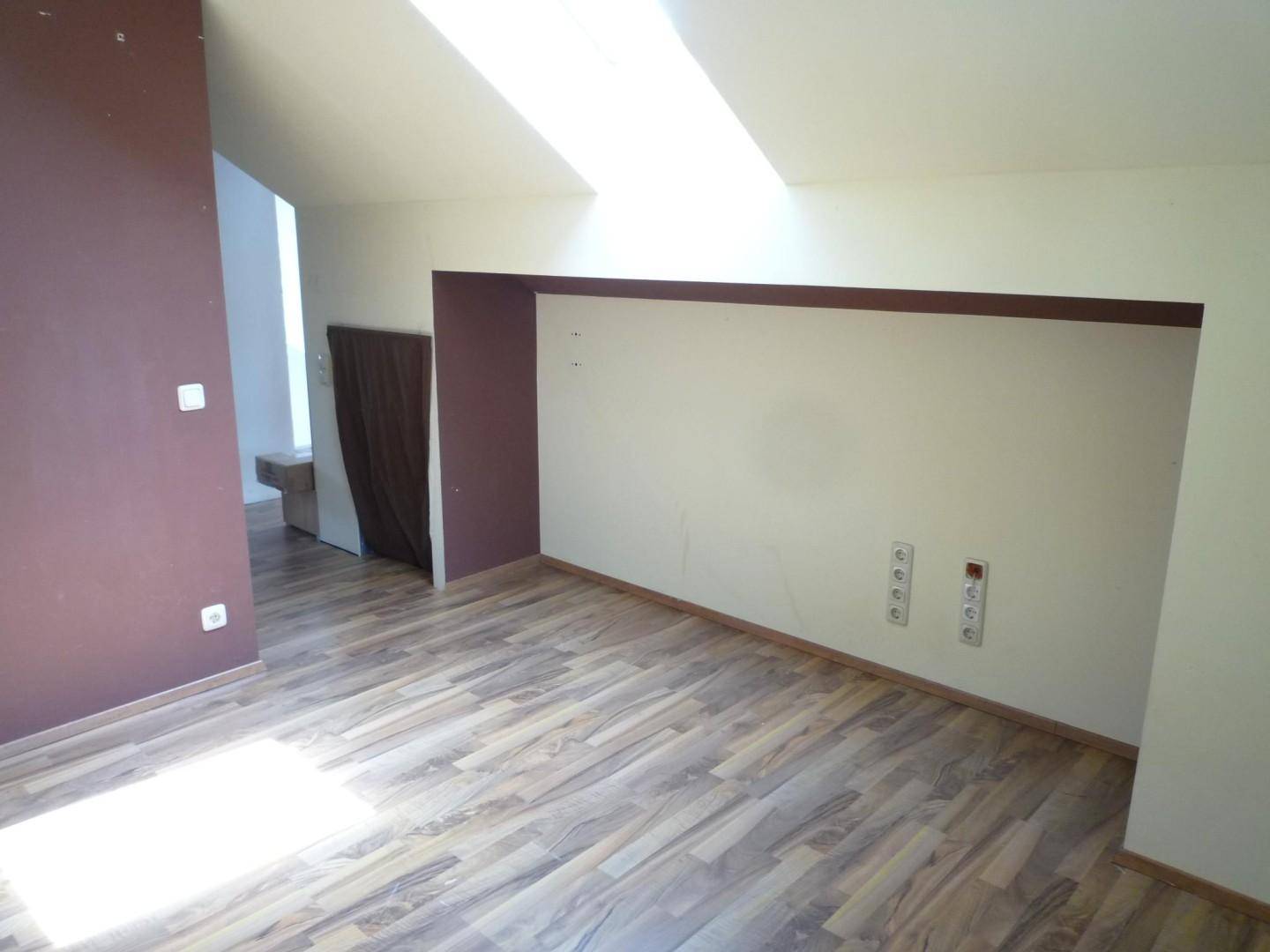 Helles Dachgeschosszimmer mit schrägen Decken, Laminatboden und Dachfenstern.