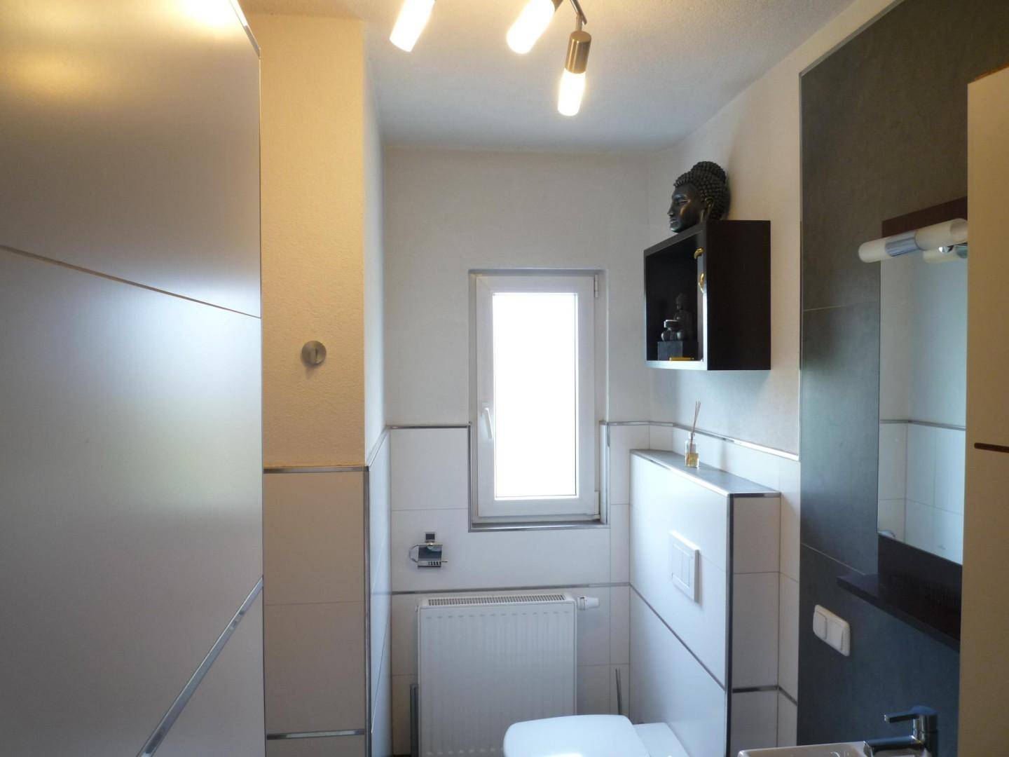 Modernes Gäste-WC mit weißen und grauen Fliesen, Fenster und Heizkörper.