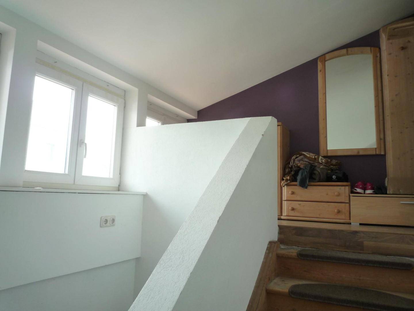 Dachgeschossraum mit schrägen Decken, Fenster und Holzmöbeln, zugänglich über eine Treppe.