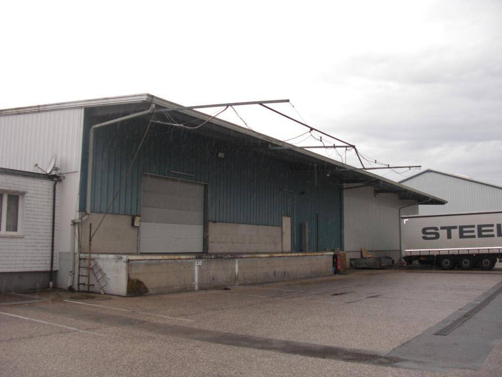Laderampe einer Lagerhalle mit Überdachung und einem abgestellten LKW-Anhänger im Industriegebiet.