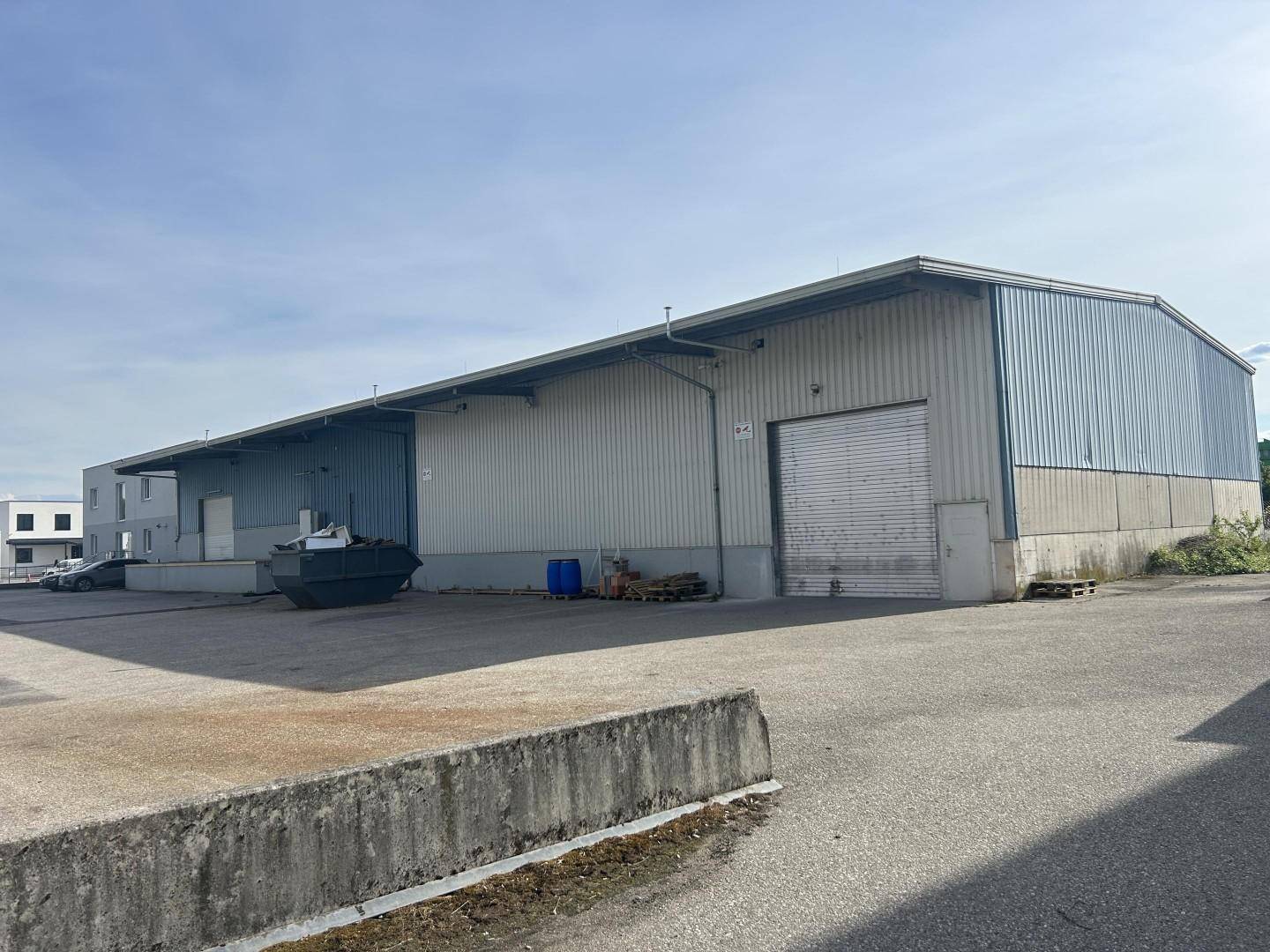 Weitläufige Außenansicht einer großen Lagerhalle mit Laderampen und einem Container auf dem Vorplatz.