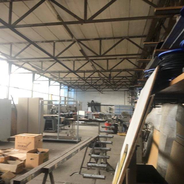 Große Industriehalle mit hohen Decken, sichtbaren Stahlträgern und viel Tageslicht durch die Fensterfronten an der Seite.